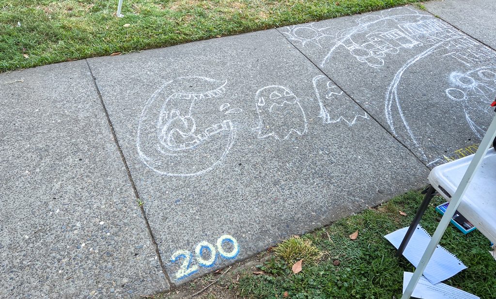 A photo of my initial sketch on the sidewalk square, showing a white outline of Pac-Man and the ghosts. The square number (200) in the lower left corner is blocked out and finished.